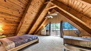 Un dormitorio acogedor en el ático, con techo inclinado, ventilador de techo y un amplio ventanal con vistas al exterior.