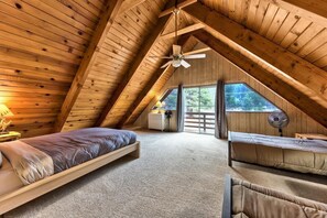 Ein gemütliches Schlafzimmer im Dachgeschoss mit schräger Decke, einem Bett, einer Bank und einem Ventilator.