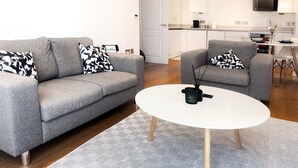 Un soggiorno moderno con un divano e una poltrona grigi, un tavolino da caffè bianco e un tappeto decorato.