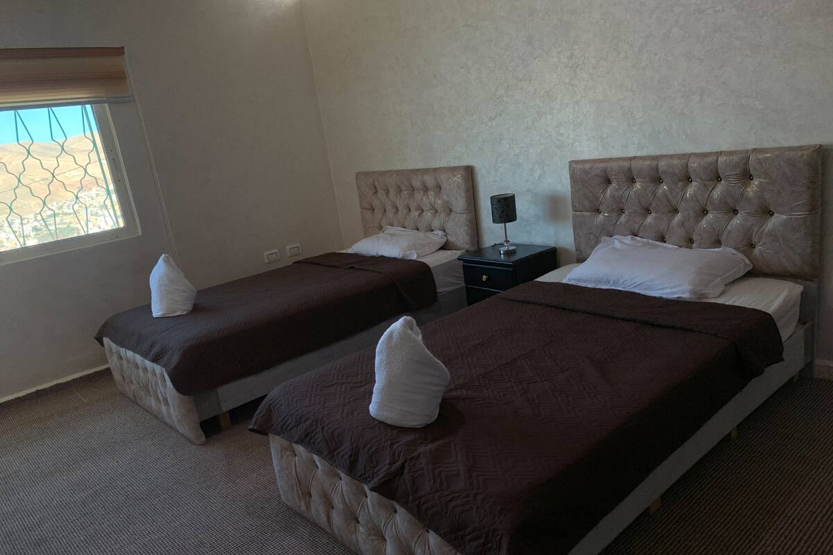 A hotel room with two beds, a nightstand, and a window with a view.