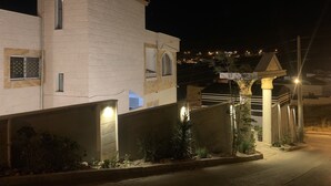 A nighttime view of a residential area with a prominent white building featuring a balcony and a small tower-like structure. - Paradise Tree  (Wadi Musa)