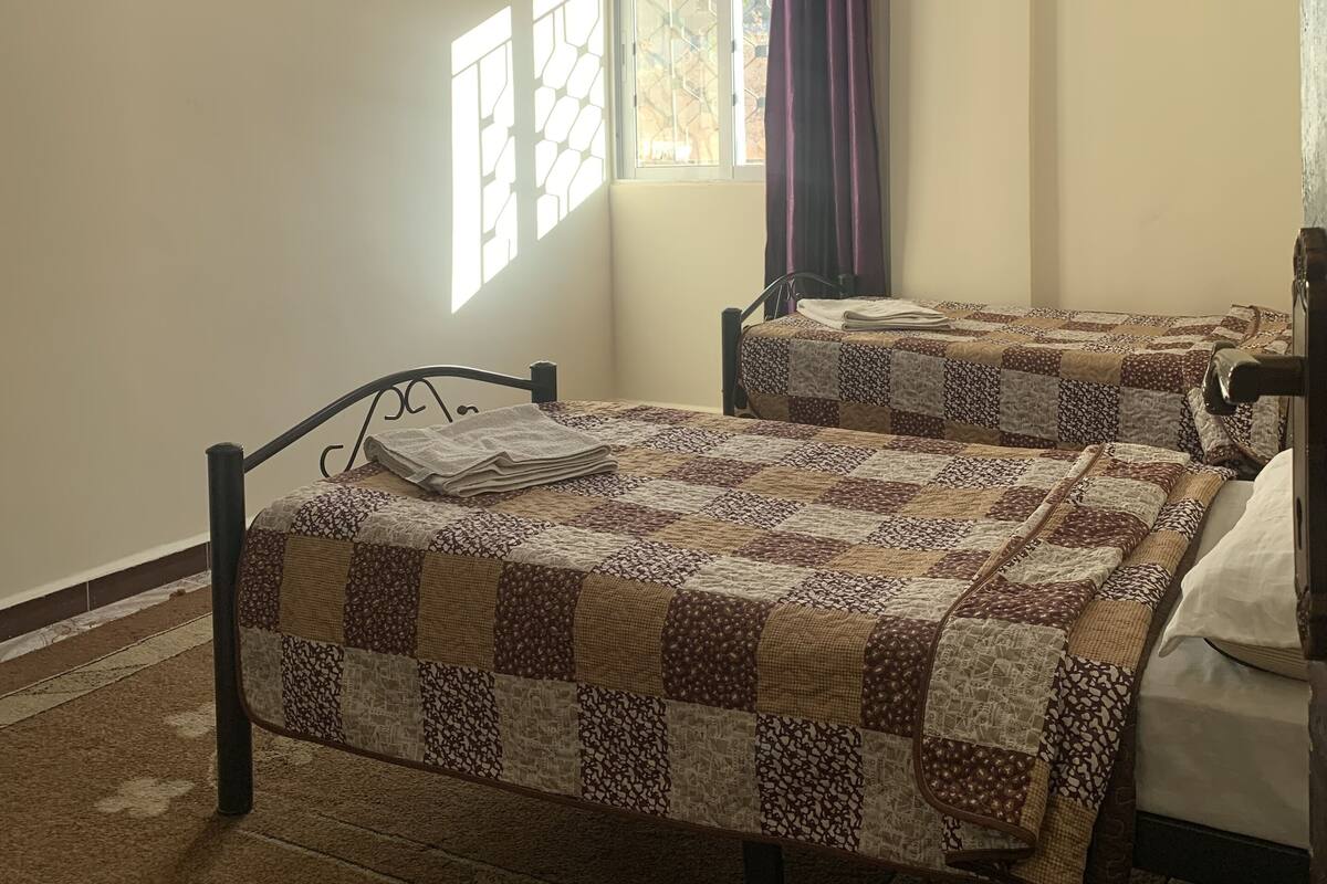 A bedroom with two beds, a window with bars, a ceiling fan, and a curtain.