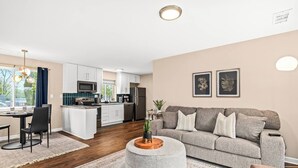 A modern living room with a grey sofa, a round coffee table, and a dining area with a table and chairs.