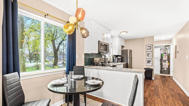 A modern kitchen with white cabinets, stainless steel appliances, and a large window offering a view of trees.