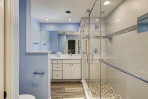 A modern bathroom with a glass shower enclosure, a vanity with a mirror, and a wooden floor. - Marsh front luxury home in Sea Pines with a screen porch and private pool. (Hilton Head Island)