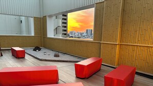 Un interior moderno con asientos rojos, un pequeño jardín y vistas de la ciudad a través de un ventanal grande.