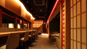 Un restaurante con una barra larga, múltiples sillas y un separador de estilo tradicional japonés.