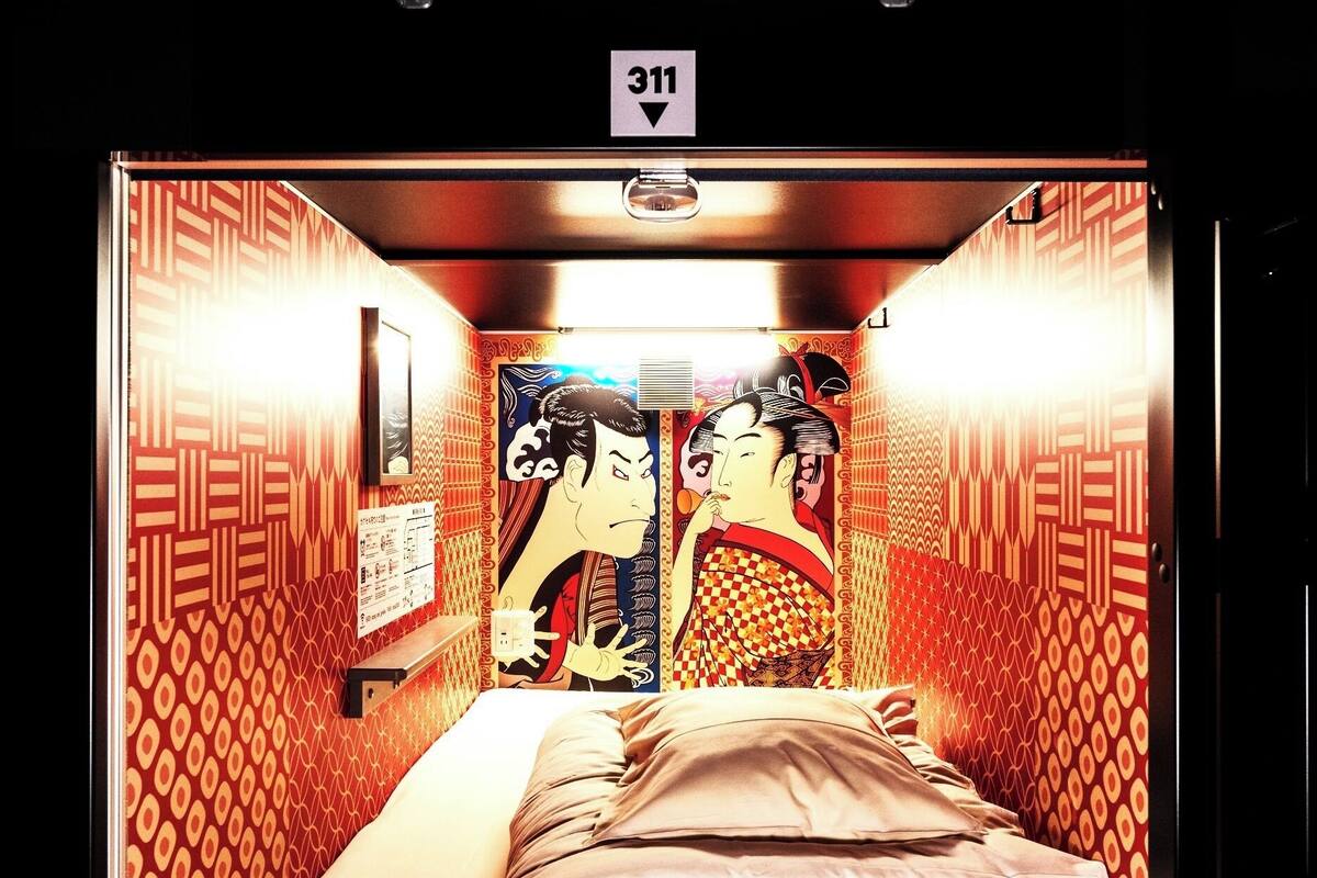 A room with a bed, a wall clock, and a door with a number sign.