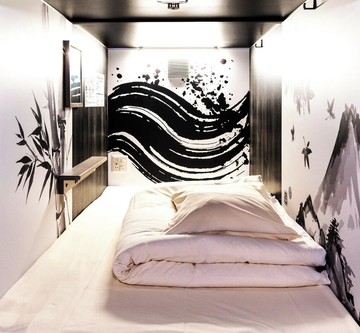 A bedroom with a bed, a wall-mounted shelf, and a wall with a black and white abstract design.