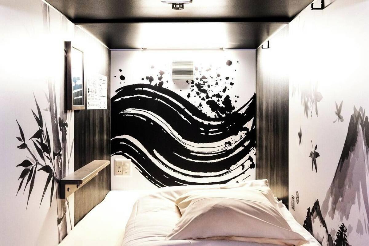 A bedroom with a bed, a wall-mounted shelf, and a wall with a black and white abstract design.