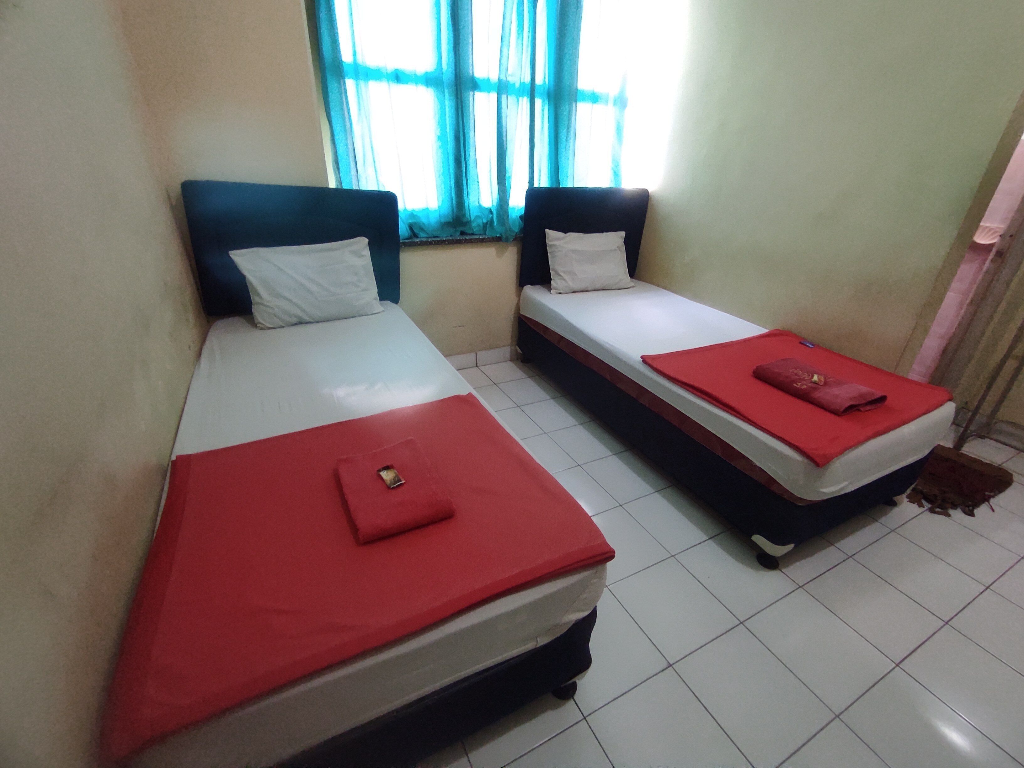 Dos camas individuales con cubrecamas rojos y almohadas blancas en una habitación con suelo de baldosas.
