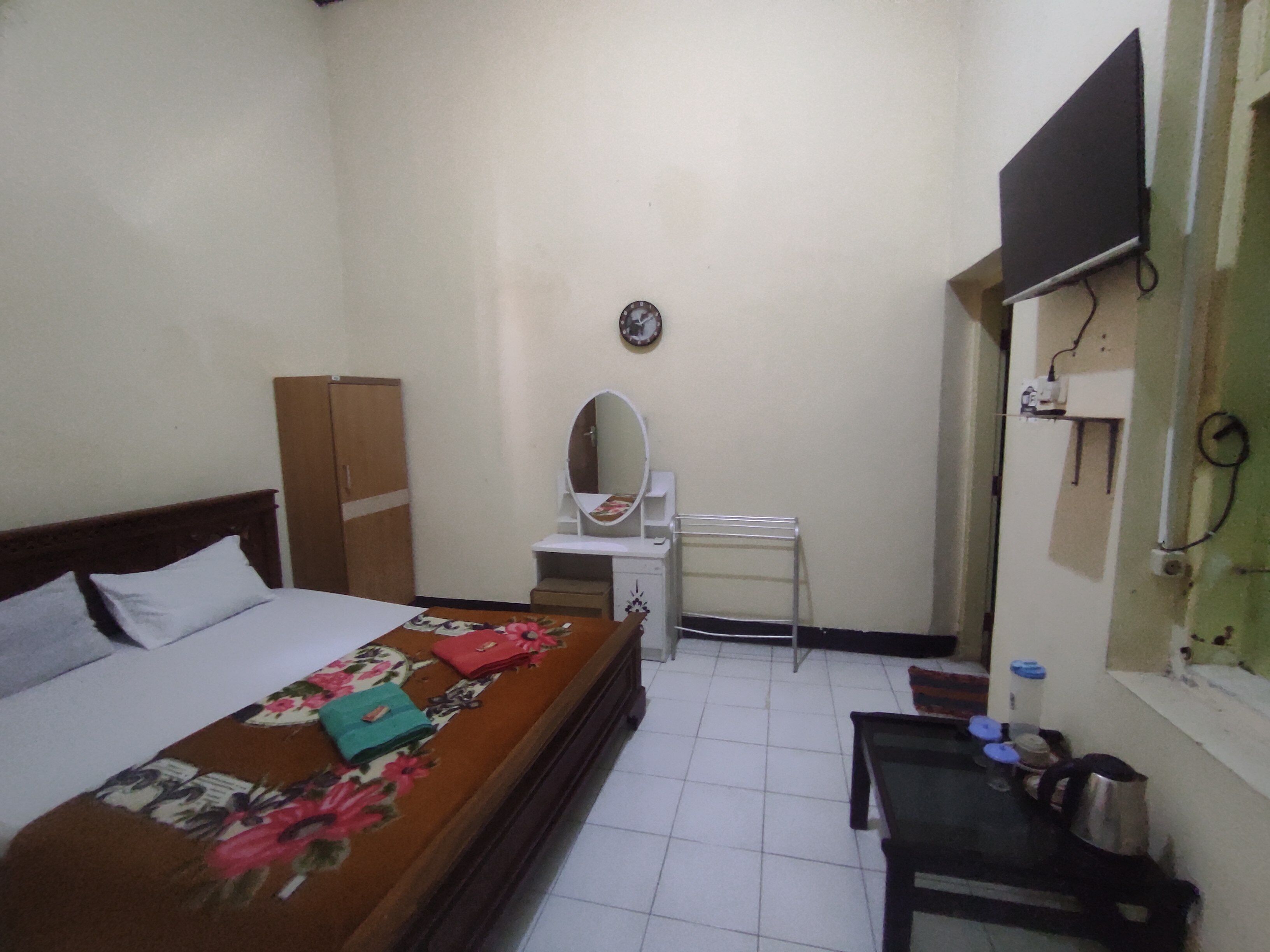 A small, clean room with a bed, a desk, a chair, a mirror, and a TV mounted on the wall.