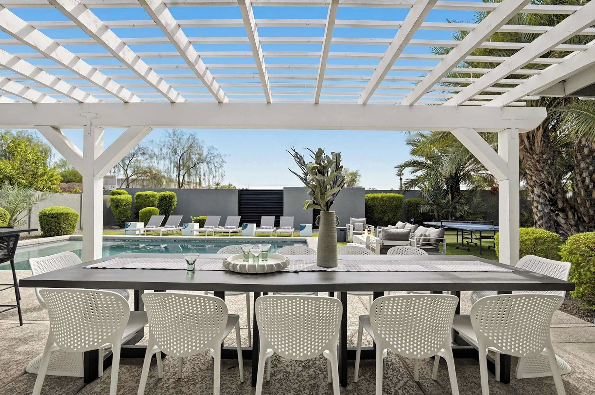 A covered outdoor dining area with a pool in the background.