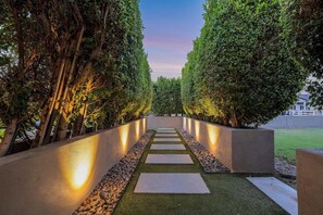 A pathway flanked by trees and illuminated walls, leading to a building. - Indigo Oasis, Pool,  Sleeps 18 (Phoenix)