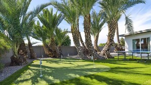 A well-maintained golf course with lush green grass, palm trees, and a modern building in the background.