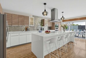 A modern kitchen with a central island, white cabinetry, and a dining area with white chairs. - Indigo Oasis, Pool,  Sleeps 18 (Phoenix)