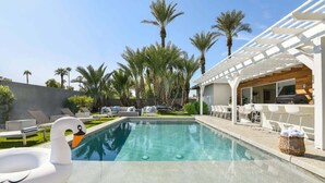 A swimming pool with lounge chairs and a pergola, surrounded by palm trees.