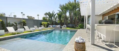 A swimming pool with lounge chairs, a pergola, and a basket of towels.