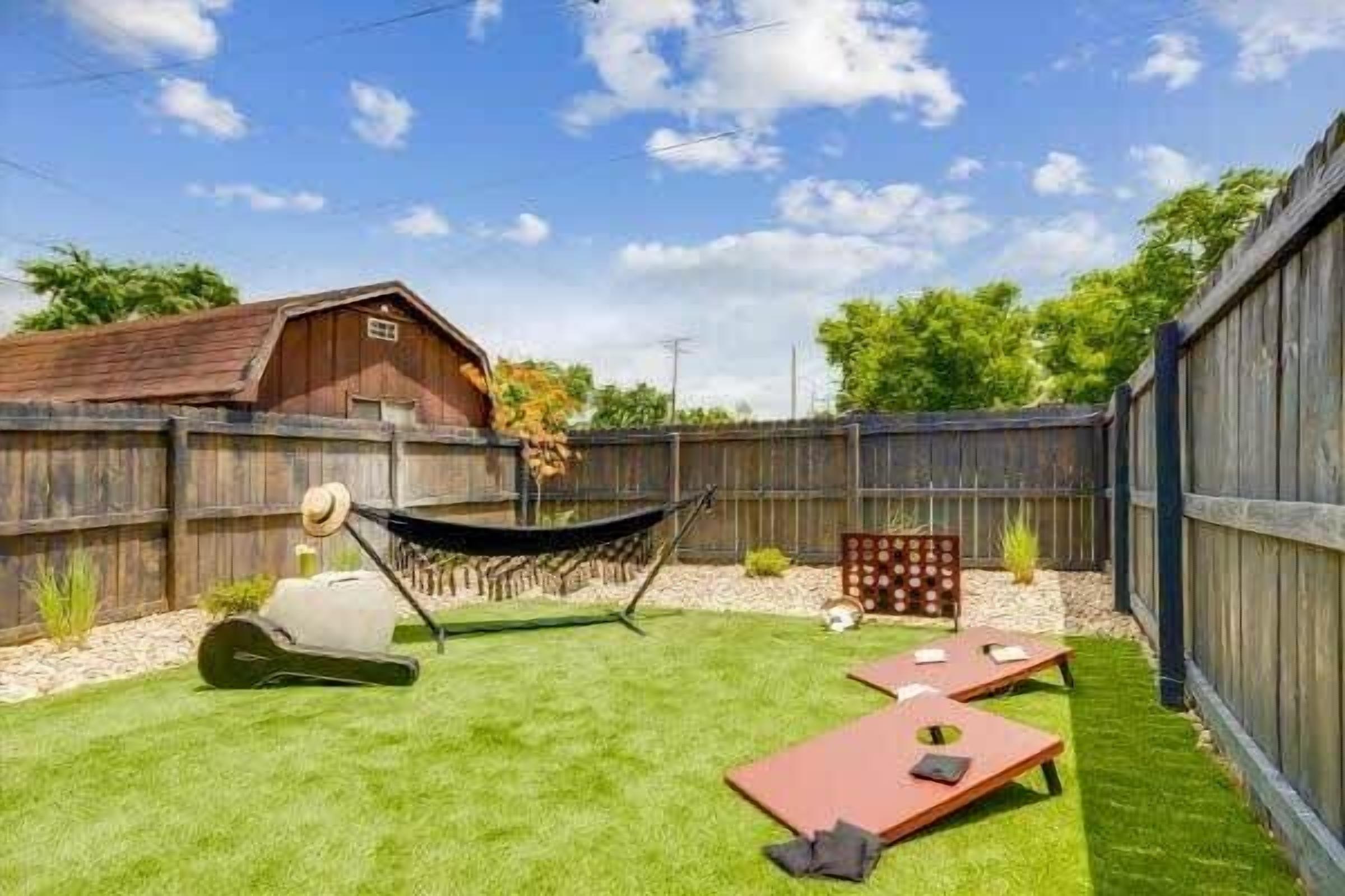 A backyard with a hammock, two sun loungers, a barbecue grill, and a wooden fence.