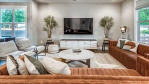 Ein modernes Wohnzimmer mit einem großen Flachbildfernseher, einem braunen Ledersofa, einem weißen Couchtisch und einem weißen Schrank.