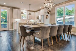 A modern kitchen with a central island, dark wood flooring, and a large window providing a view of the outdoors. - Private Single Family Luxury Home | Hot Tub (Nashville)