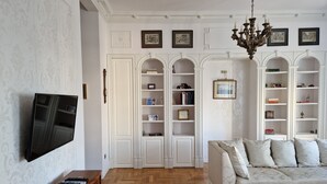 A living room with a sofa, wooden floor, white walls, and a TV mounted on the wall. - Luxury Living Kopernik (Warszawa)