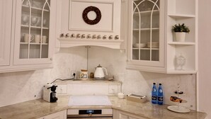 A kitchen with white cabinetry, a built-in oven, a coffee maker, and a kettle on the countertop. - Luxury Living Kopernik (Warszawa)