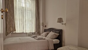 A bedroom with a bed, a nightstand, a lamp, and a window with curtains. - Luxury Living Kopernik (Warszawa)