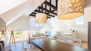 Ein stilvolles Loftzimmer mit Holztisch, weißen Stühlen und einem großen Fenster mit Blick ins Freie.