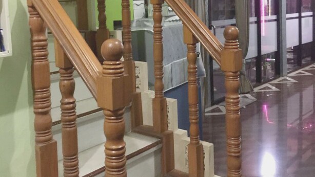 A staircase with wooden balusters and a handrail, leading to a room with a green wall and a window with curtains. - OYO Life 93055 Fathin Hotel (Sangkapura)