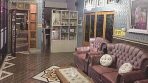 A hotel lobby with a leather sofa, a patterned rug, and a bookshelf with various items. - OYO Life 93055 Fathin Hotel (Sangkapura)