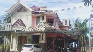A two-story house with a covered porch and a car parked in front. - OYO Life 93055 Fathin Hotel (Sangkapura)