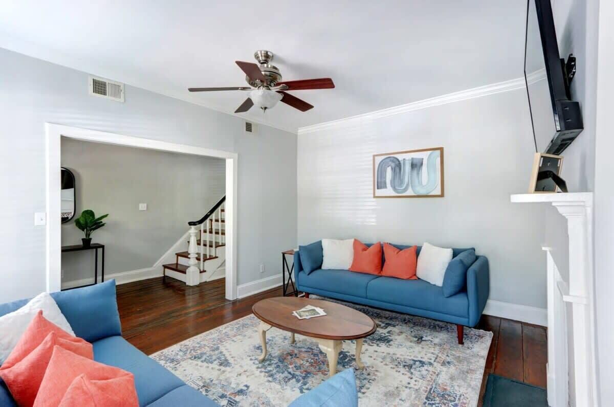 Ein Wohnzimmer mit blauem Sofa, Couchtisch, Deckenventilator und einer Treppe, die in einen anderen Raum führt.