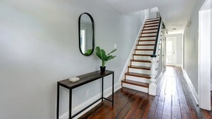 A hallway with a wooden staircase, a console table with a plant, and a mirror on the wall. - The Tea Olive - A, Fresh | Updated | Dog-Friendly (Savannah)