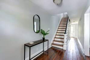 A hallway with a wooden staircase, a console table with a plant, and a mirror on the wall. - The Tea Olive - A, Fresh | Updated | Dog-Friendly (Savannah)