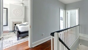 A bedroom with a bed, a ceiling fan, and a patterned wall decoration. - The Tea Olive - A, Fresh | Updated | Dog-Friendly (Savannah)