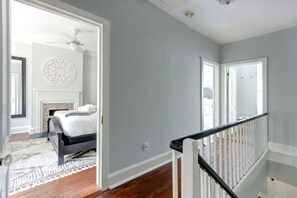 A bedroom with a bed, a white ceiling fan, a patterned wall decoration, and a wooden floor. - The Tea Olive - A, Fresh | Updated | Dog-Friendly (Savannah)