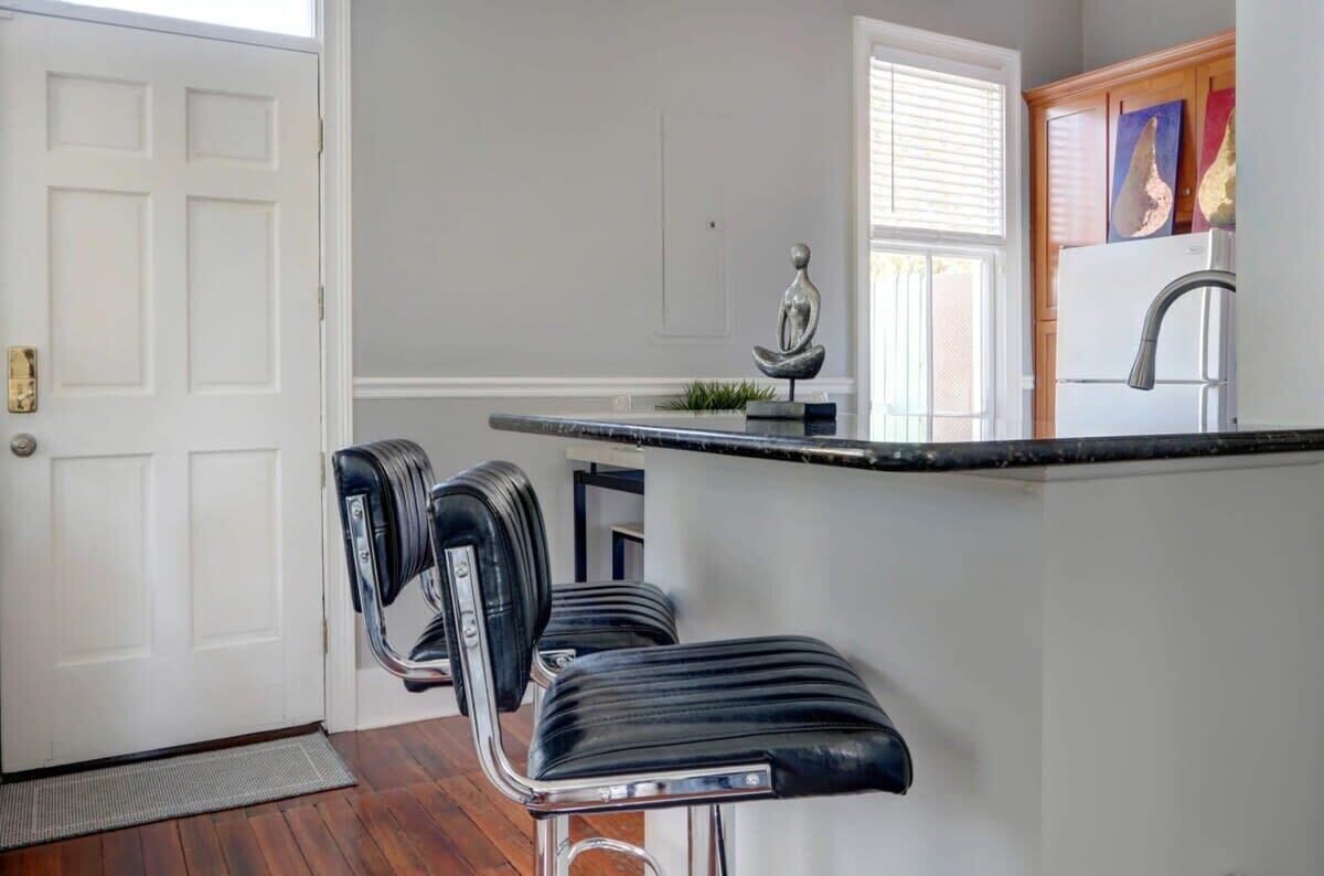 A kitchen with a white door, a black bar stool, a white refrigerator, and a window with blinds.