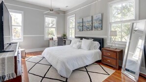 A bedroom with a bed, a desk, a chair, a dresser, a TV, and artwork on the wall. - Historic 1800's Condo, Forsyth | Dog-Friendly! (Savannah)
