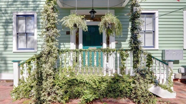 A green house with a white porch, a green door, and a white railing. - Historic 1800's Condo, Forsyth | Dog-Friendly! (Savannah)