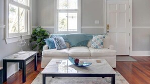 A living room with a white sofa, a coffee table, and a potted plant. - Historic 1800's Condo, Forsyth | Dog-Friendly! (Savannah)