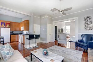 A modern living room with a marble coffee table, a sofa, and a blue leather chair. There is a kitchen area with wooden cabinets and a microwave.