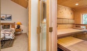 A cozy room with a bed, a nightstand, a lamp, and a wooden sauna.