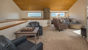 A cozy living room with a pool table, leather chairs, a stone fireplace, and a couch.