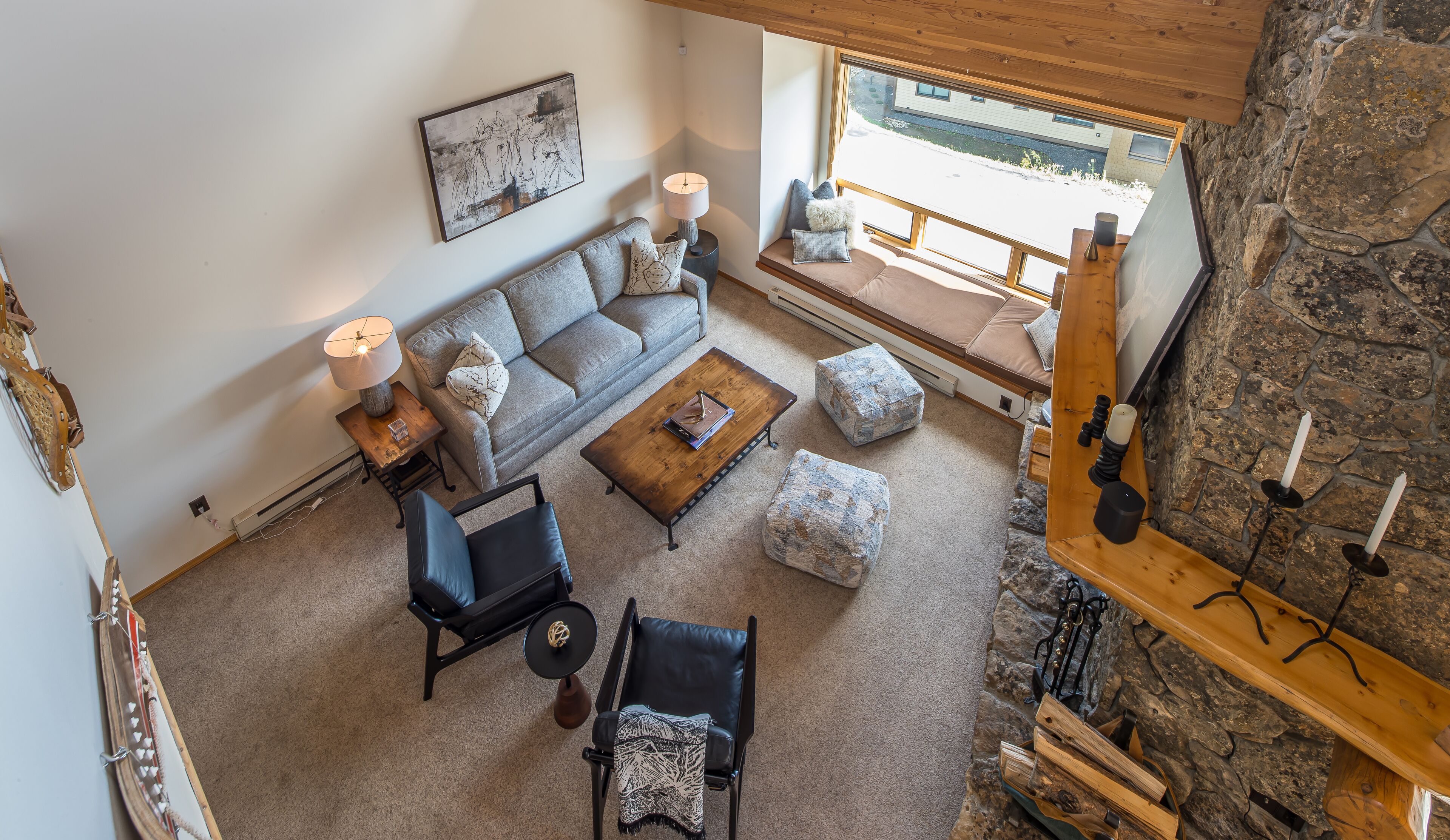 A cozy living room with a sofa, coffee table, and chairs, a fireplace with candles, and a stone wall.