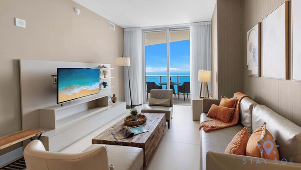 A modern hotel room with a large TV, comfortable seating, a balcony with a view of the sea, and a well-lit space. - Upper Level Penthouse: Beach & Intercostal Views (Hollywood)