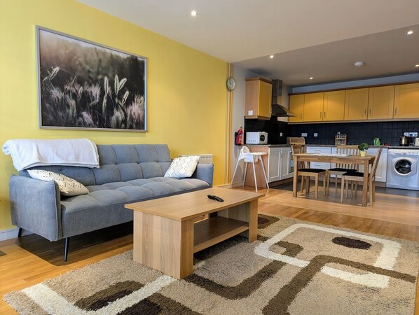 A modern living room with a sofa, coffee table, and a dining area with chairs and a table.