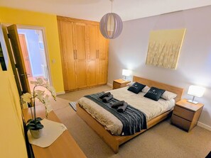 Un dormitorio con cama, mesitas de noche, un armario, una planta en maceta y una obra de arte colgada en la pared.