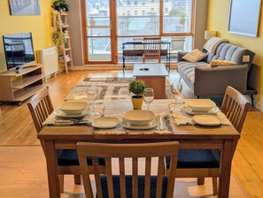 A dining area with a wooden table set for four, surrounded by chairs, with a view of the city through large windows. - 12 Courthouse Square Apt with Parking (Clifden)