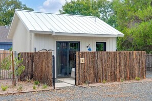 A small, single-story building with a white exterior and a sloped metal roof. There is a wooden fence in front, and a small number '2' sign on the fence. - The Stables at The Homestead (Fredericksburg)